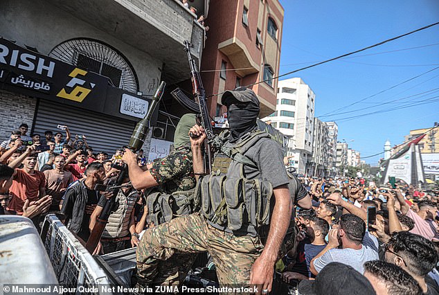 Palestinian militants brandish weapons as they pass through Israeli territory on trucks