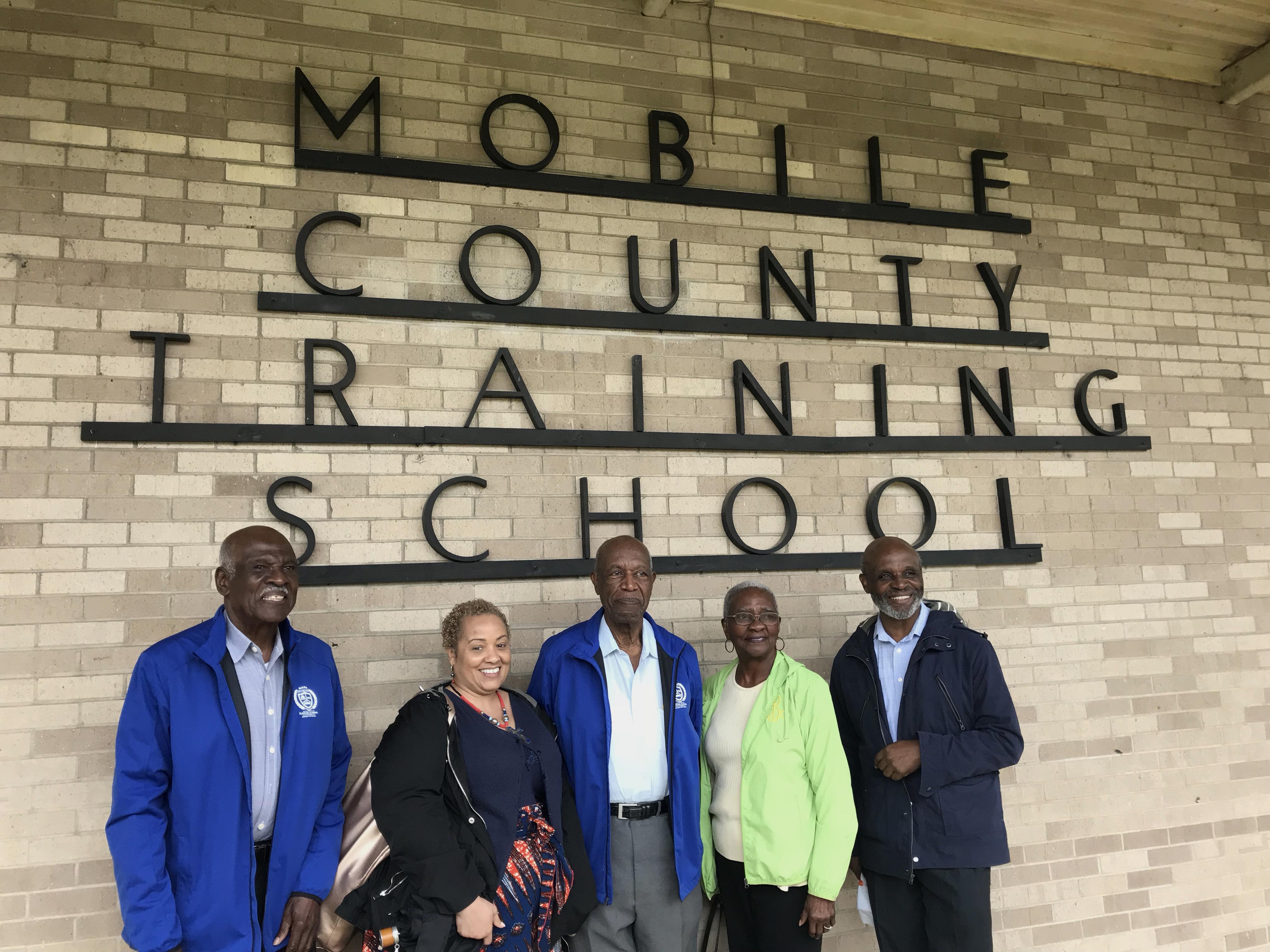 A group of people standing under the Mobile County Training School sign.