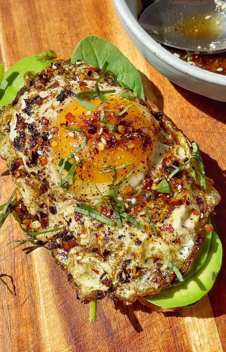 One fried egg on toast with chili crisp oil drizzled and chopped basil on top.
