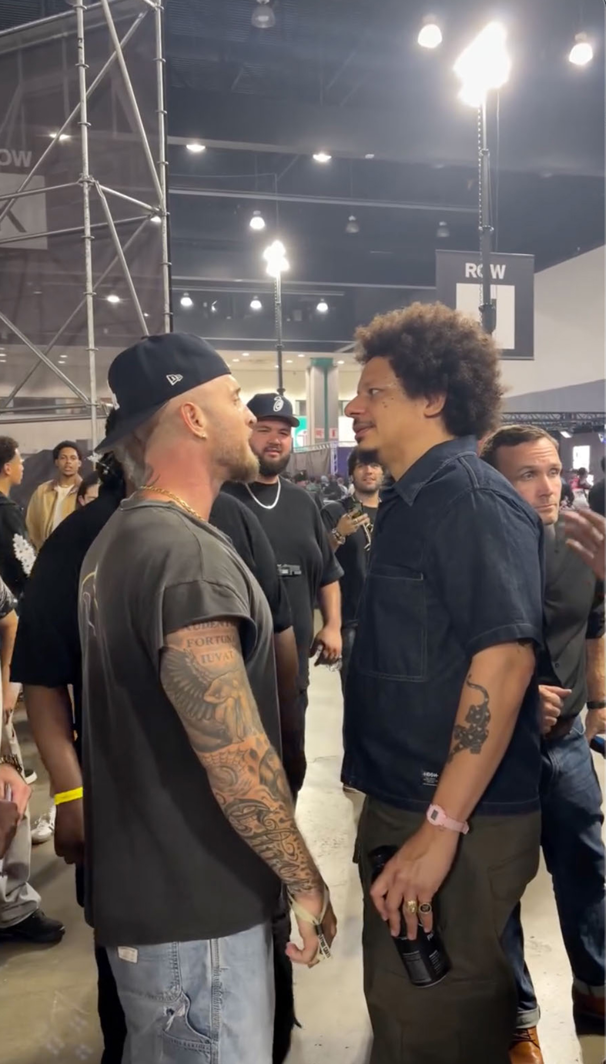 Chet Hanks and Eric Andre standing face to face in a crowded convention hall.