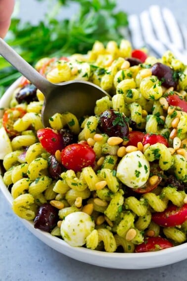 Pesto pasta salad with cherry tomatoes, olives, mozzarella balls, pine nuts and red onion. Pesto pasta salad with cherry tomatoes, olives, mozzarella balls, pine nuts and red onion.