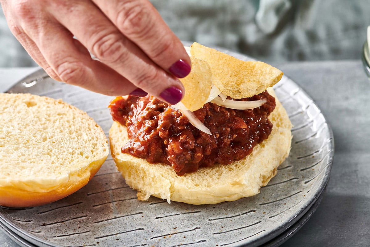 Topping sloppy joe sandwich with onions and potato chips.