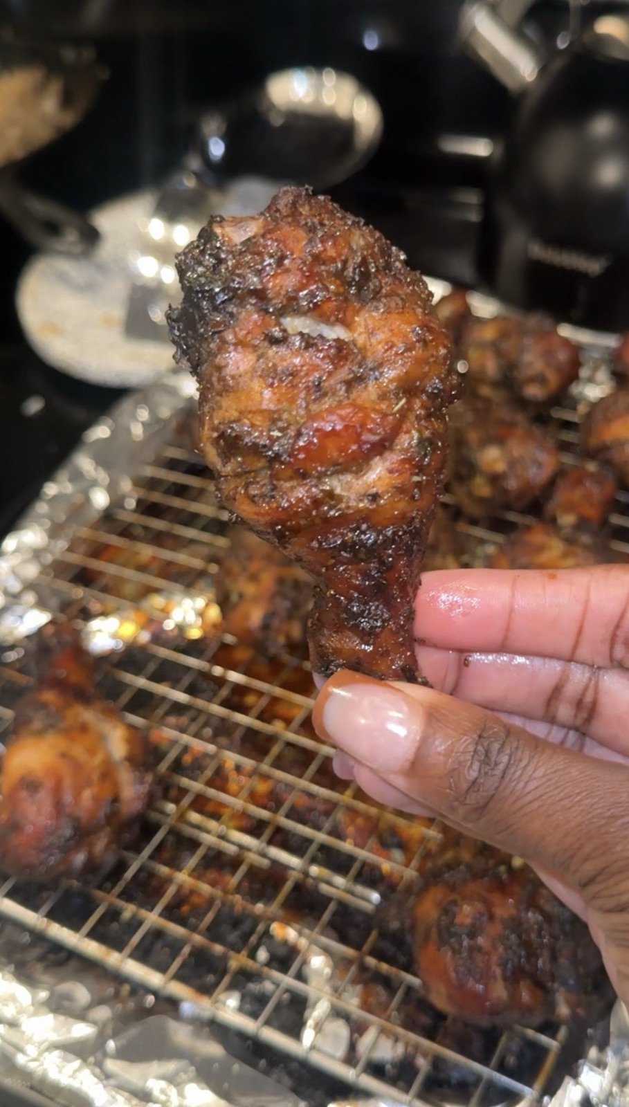 Hand holding a single oven-grilled drumstick showing dark caramelized char