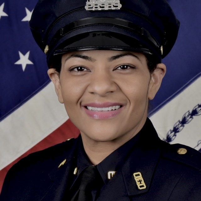 NYPD Detective Ada Reyes in uniform smiling in front of an American flag.