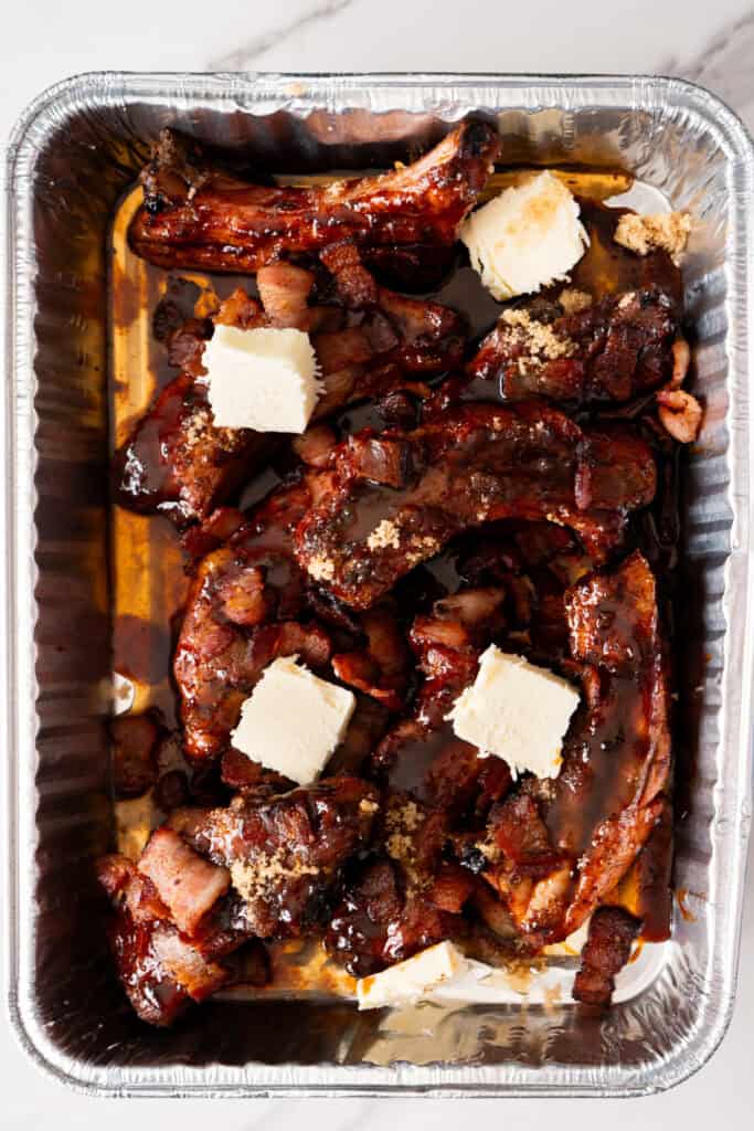 Smoked maple bacon party ribs in a foil pan.