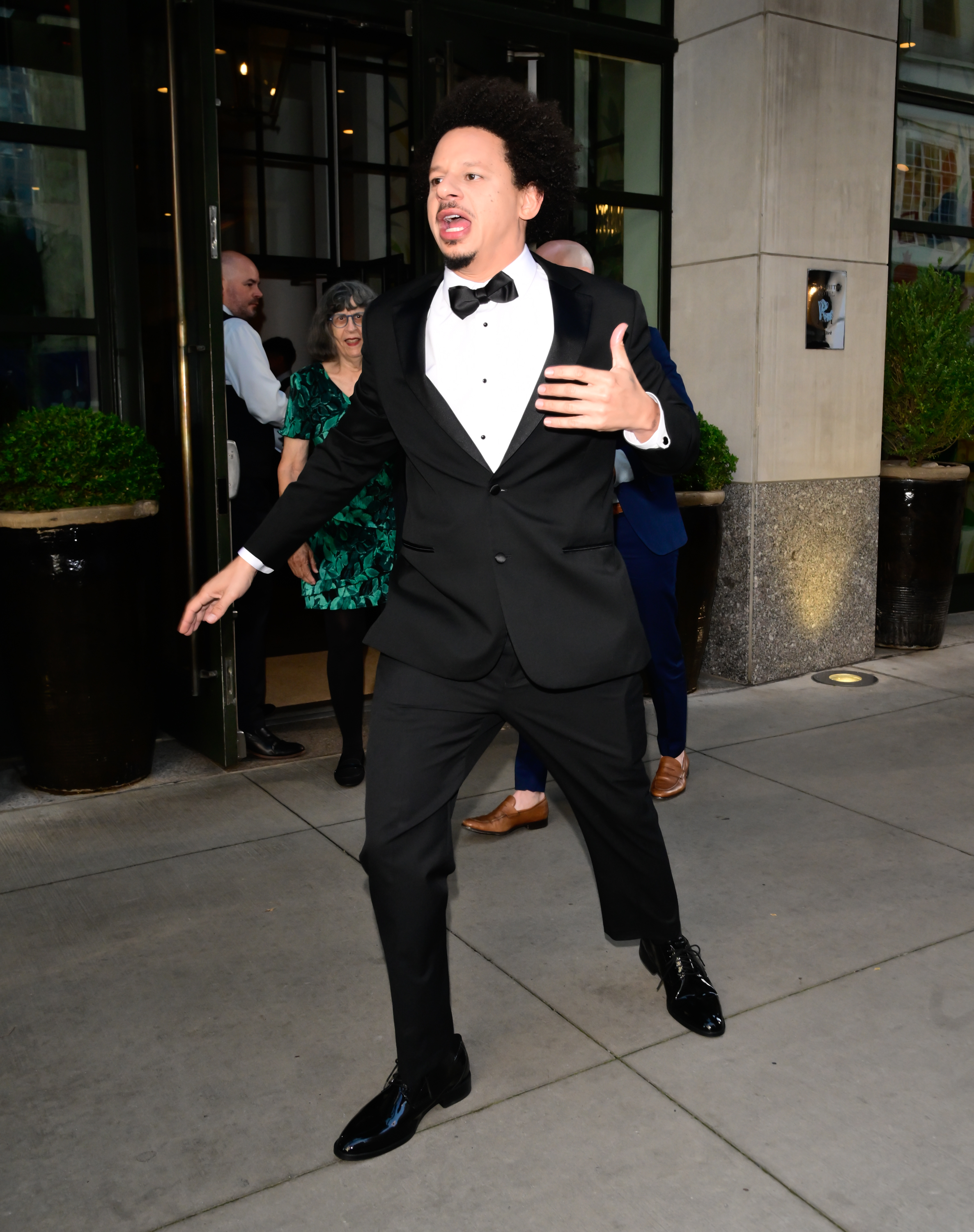 Eric André wearing a tuxedo outside a building in New York City.