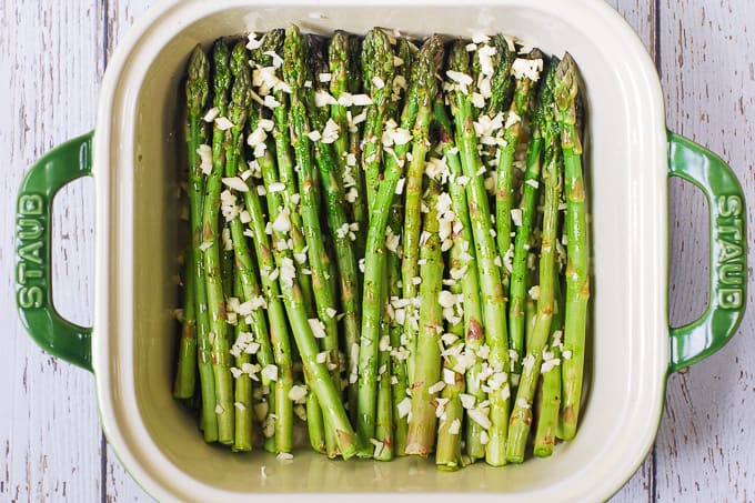 Asparagus drizzled with olive oil, seasoned with salt and pepper, and topped with fresh minced garlic in a white casserole dish