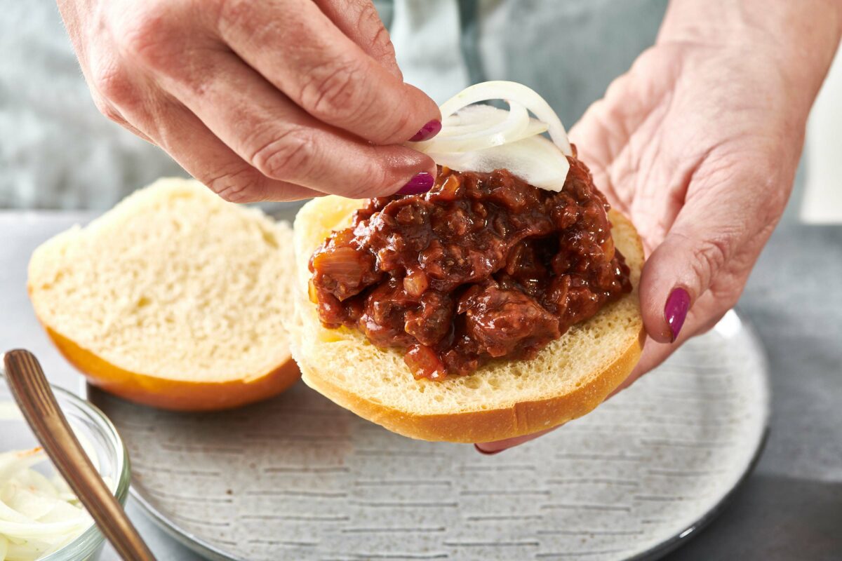 Adding slice onion to sloppy Joe sandwich on bun.