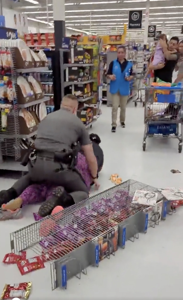 The cop is seen trying to restrain the woman, sitting on her