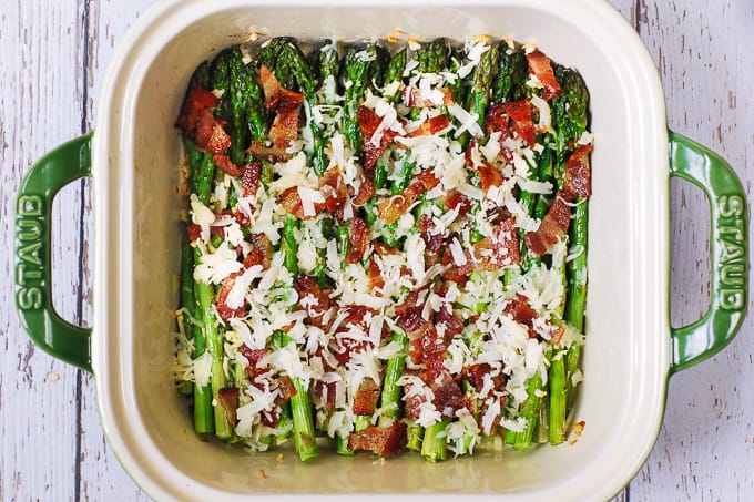 Asparagus with shredded cheese and cooked bacon in a casserole dish