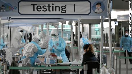 Medical staff wearing protective clothing take test samples for the Covid-19 coronavirus from a foreign passenger at a virus testing booth outside Incheon international airport, west of Seoul, on April 1, 2020. 