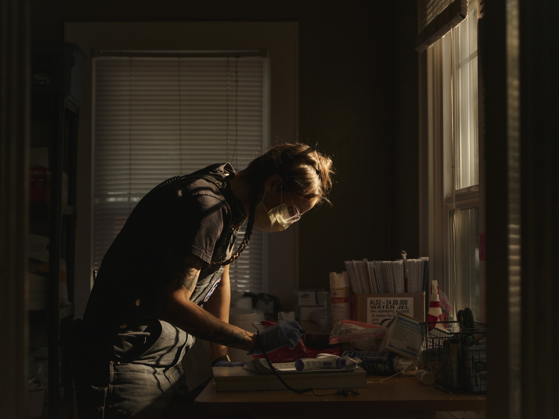 A medic leans over a desk in a darkened room, preparing medical supplies.