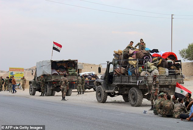 Military vehicles transporting Syrian regime troops and rolled up mattresses are stationed on the outskirts of the northern Syrian border town of Kobane