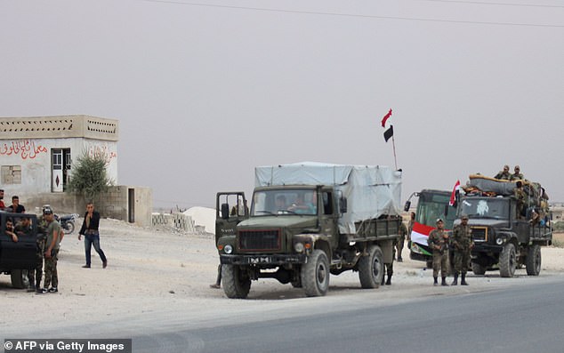 A convoy of military vehicles and busses transporting Syrian regime troops are stationed on the outskirts of the northern Syrian border town of Kobane yesterday