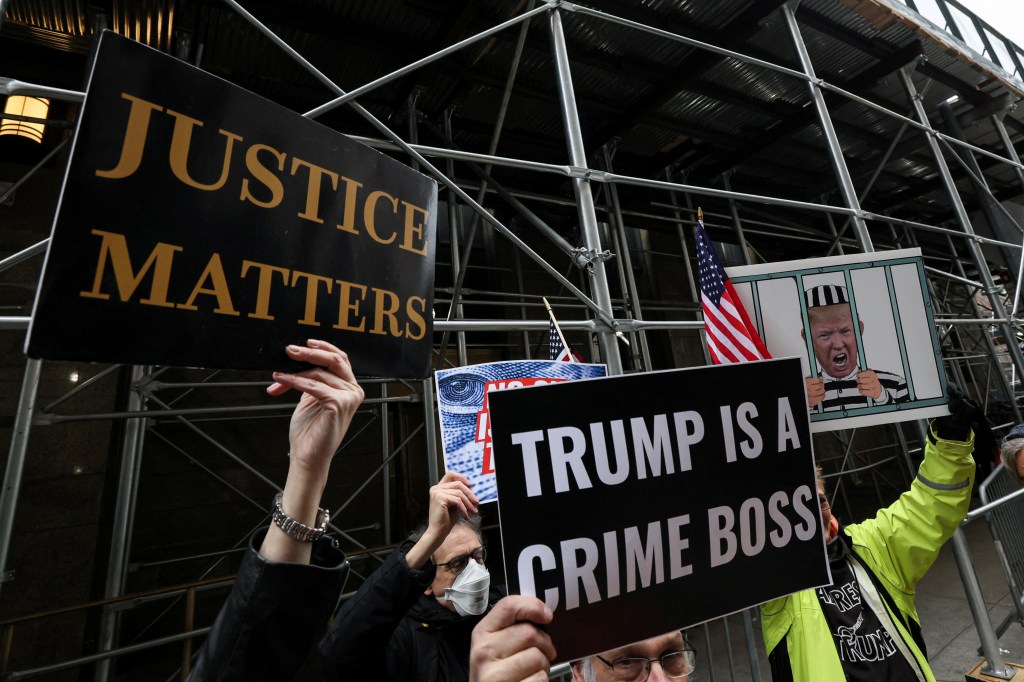 Anti-Trump protestors hold a placards outside Manhattan District Attorney Alvin Bragg's office.