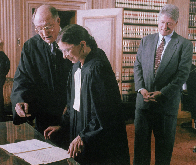 As President Bill Clinton looks on, Chief Justice William Rehnquist helps the Supreme Court's newest member, Ruth Bader Ginsburg, sign the court's oath card, on Oct. 1, 1993.