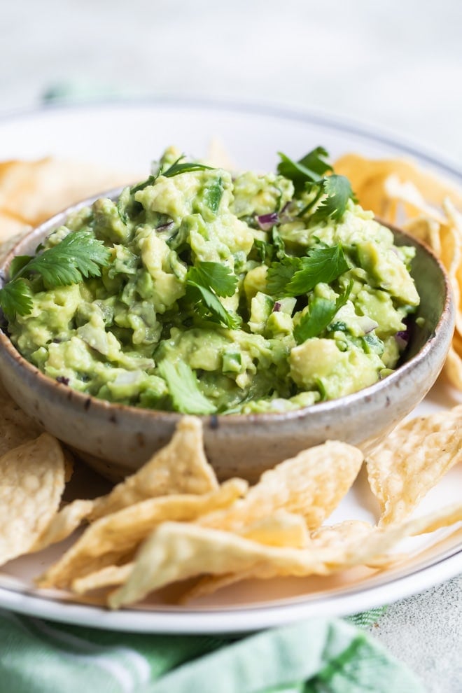 Chipotle guacamole in a brown dish on a white platter with tortilla chips.