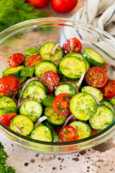 A bowl of cucumber tomato salad garnished with fresh herbs. A bowl of cucumber tomato salad garnished with fresh herbs.